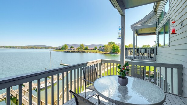 Eine Terrasse mit Tisch und Stühlen mit Blick auf einen See, an dem ein Steg und Boote liegen.