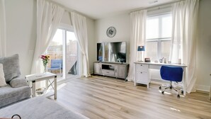 A modern living room with a sofa, a TV, a desk, and a chair. - Patio & Grill: Modern Family Home in Hampstead (Hampstead)