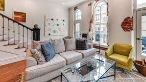 A living room with a sofa, armchair, and coffee table. There is a staircase with a railing and a door with a brick wall. - Steps to Historic Riverfront: Chic Dtwn Condo! (Paducah)