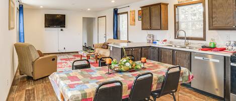 A compact kitchen with a dining area, wooden flooring, and a TV mounted on the wall.