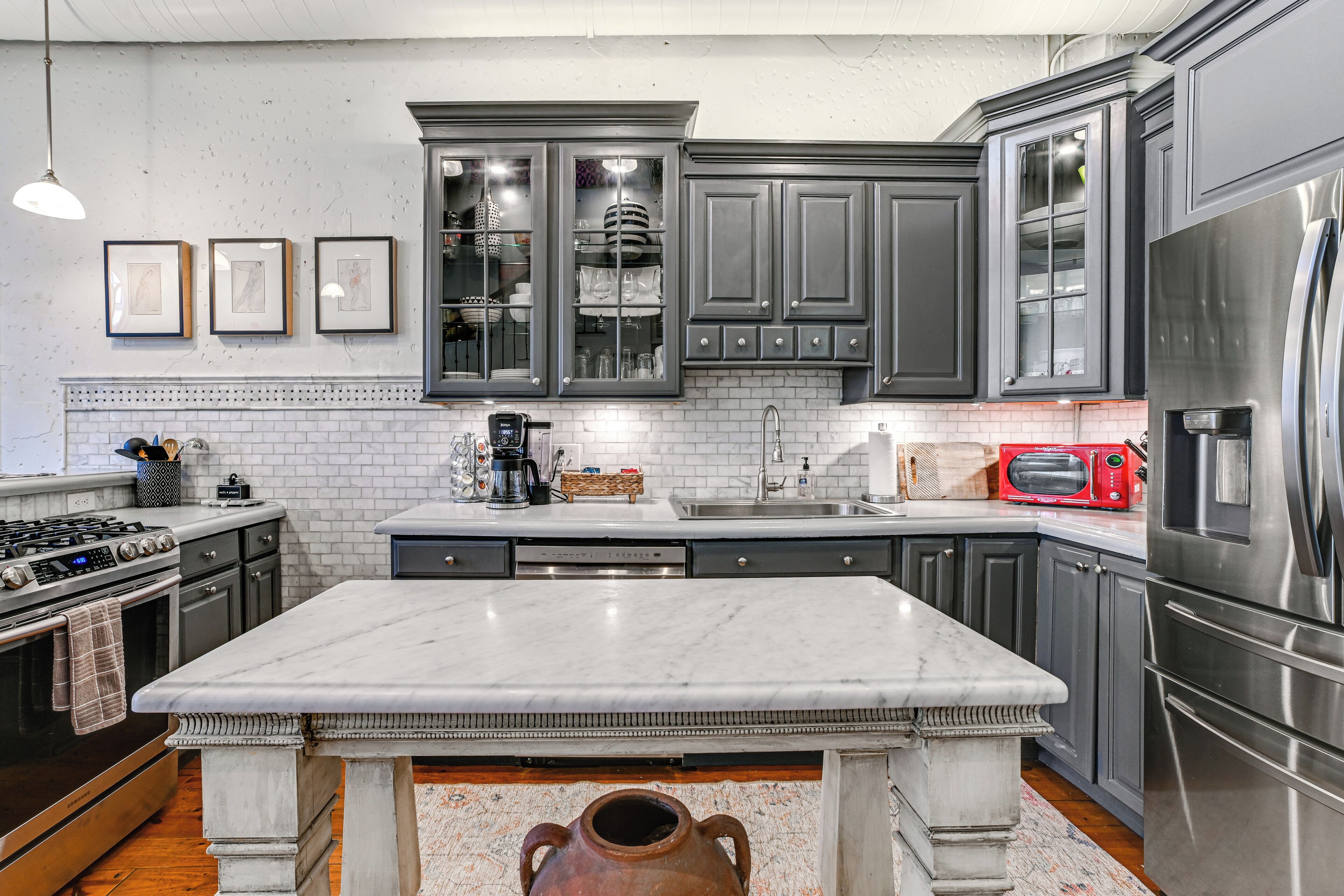 A modern kitchen with dark gray cabinets, a white marble countertop, stainless steel appliances, and a tiled backsplash.