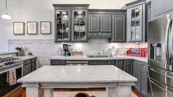A modern kitchen with dark gray cabinets, a white marble countertop, stainless steel appliances, and a tiled backsplash.