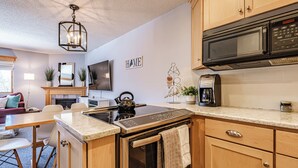 A modern kitchen with a built-in oven, microwave, and coffee maker. There is a wooden cabinet, a countertop, and a hanging light fixture. - On Mountain two bedroom condo (Newry)