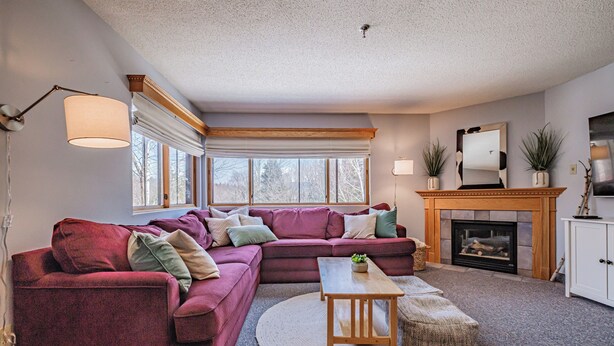 A living room with a sectional sofa, a fireplace, and a large window. - On Mountain two bedroom condo (Newry)