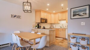 A modern kitchen with wooden cabinets, a central island, and a dining area with white chairs. - On Mountain two bedroom condo (Newry)