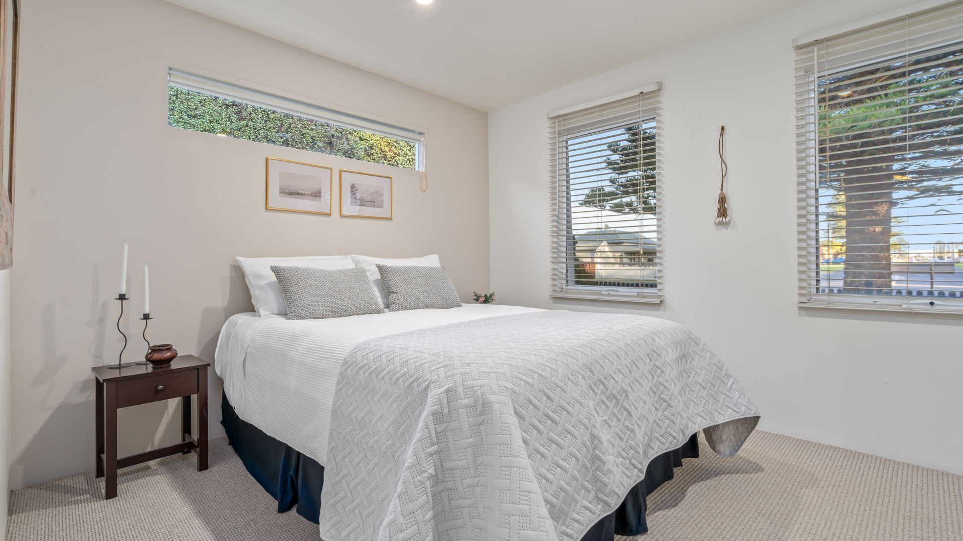 A bedroom with a bed, a nightstand, a window with blinds, and framed pictures on the wall.