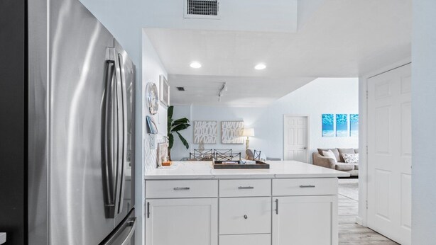 A modern kitchen with white cabinetry, a stainless steel refrigerator, and a central island.