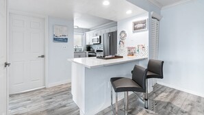 A modern kitchen with white cabinets, a stainless steel refrigerator, and a white island with two bar stools.