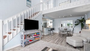 A spacious living room with a staircase, a television, a sofa, and a dining area.