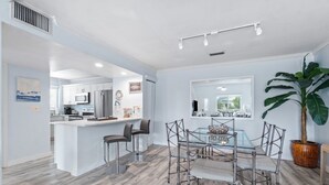 A spacious kitchen with white cabinets, a central island, and a dining area with a glass table and metal chairs.