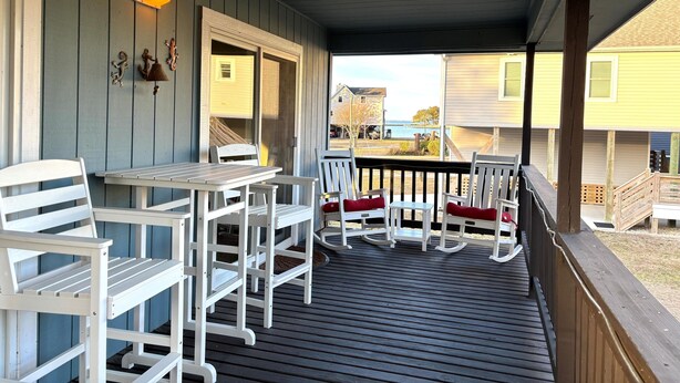 A covered porch with white wooden furniture, including a table and chairs, and a rocking chair. - CH108A- CF w/ 3 Bedrooms, Private Dock, Fire Pit and Dog Friendly (Kill Devil Hills)