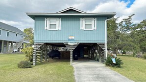 A two-story house with a covered garage entrance, a sign indicating it's for rent, and a small covered outdoor seating area. - CH108A- CF w/ 3 Bedrooms, Private Dock, Fire Pit and Dog Friendly (Kill Devil Hills)