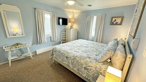 A bedroom with a bed, a desk, a chair, a TV, and a ceiling fan. - CH108A- CF w/ 3 Bedrooms, Private Dock, Fire Pit and Dog Friendly (Kill Devil Hills)