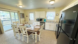 A kitchen with a dining area, white cabinets, a black refrigerator, and a view through the glass door. - CH108A- CF w/ 3 Bedrooms, Private Dock, Fire Pit and Dog Friendly (Kill Devil Hills)