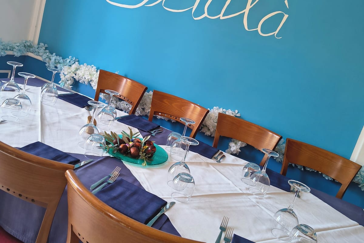 Un comedor con pared azul, sillas de madera y una mesa lista para servir una comida.
