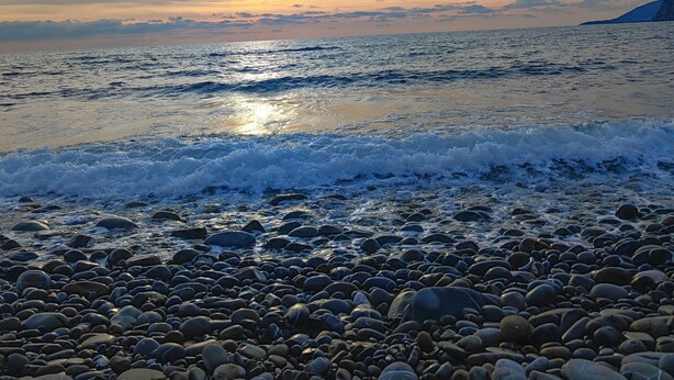 Ein felsiger Strand bei Sonnenuntergang mit Wellen.
