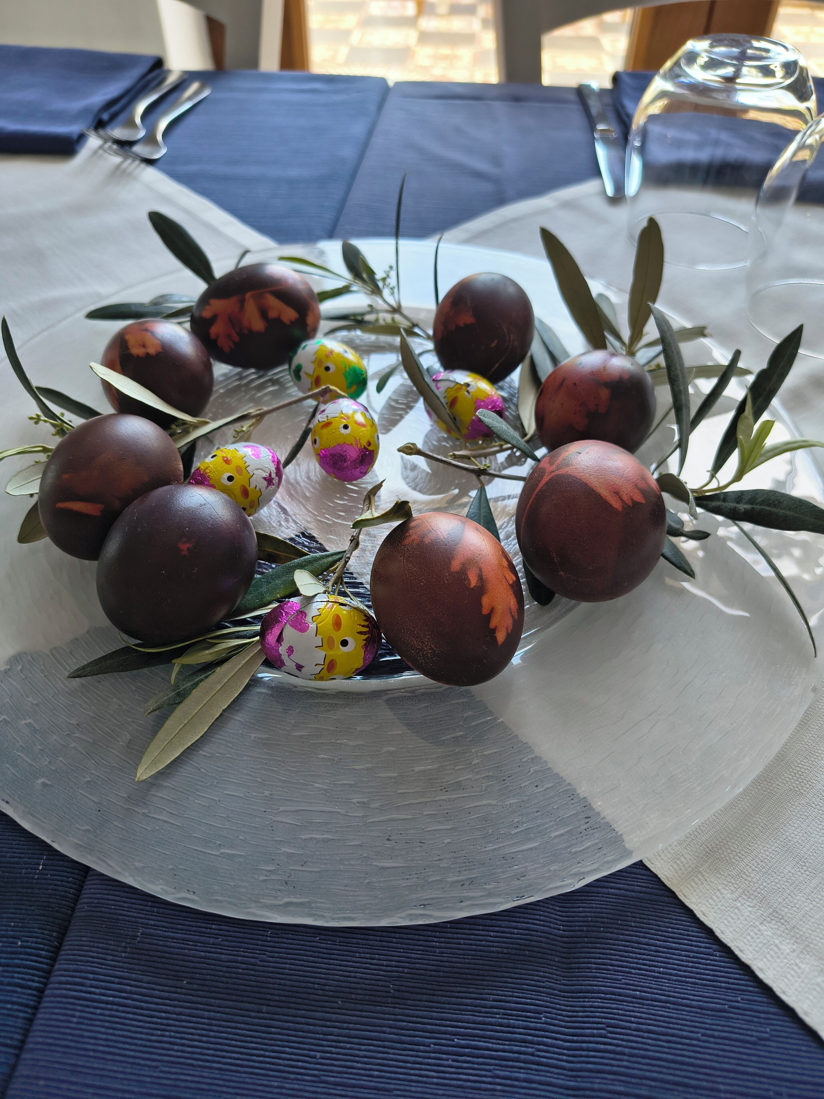 Une table ornée d’une composition décorative composée d’œufs peints et de branches d’olivier, le tout posé sur une nappe.