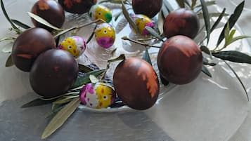 Uma mesa com arranjo decorativo de ovos pintados e ramos de oliveira, sobre uma toalha.
