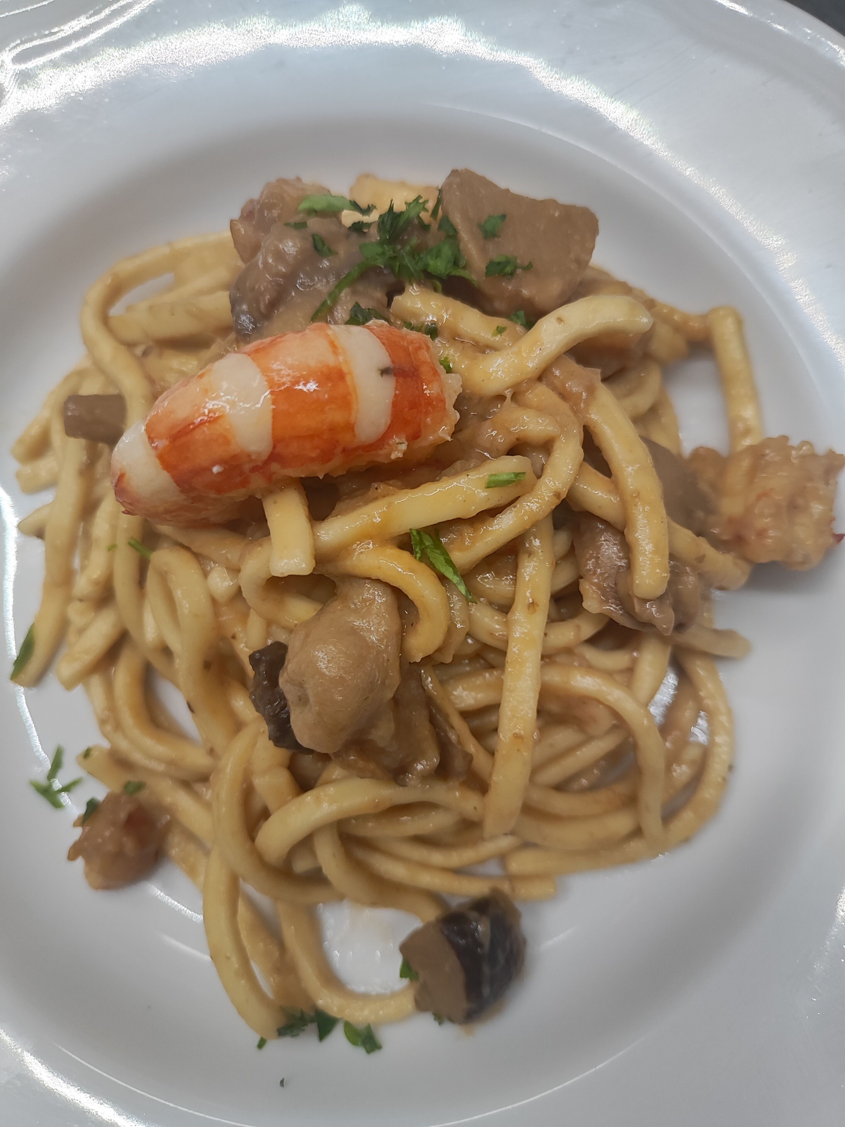 Un plato de espagueti con carne, champiñones y un camarón grande.