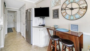 Una cocina con un reloj grande, un televisor y una zona de bar con taburetes.