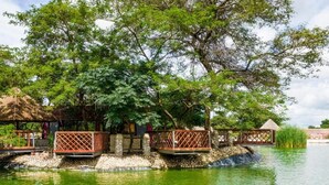 A tranquil water body with wooden walkways and a thatched-roof structure surrounded by lush greenery. - Twalumba Resort & Hotel (Lusaka)