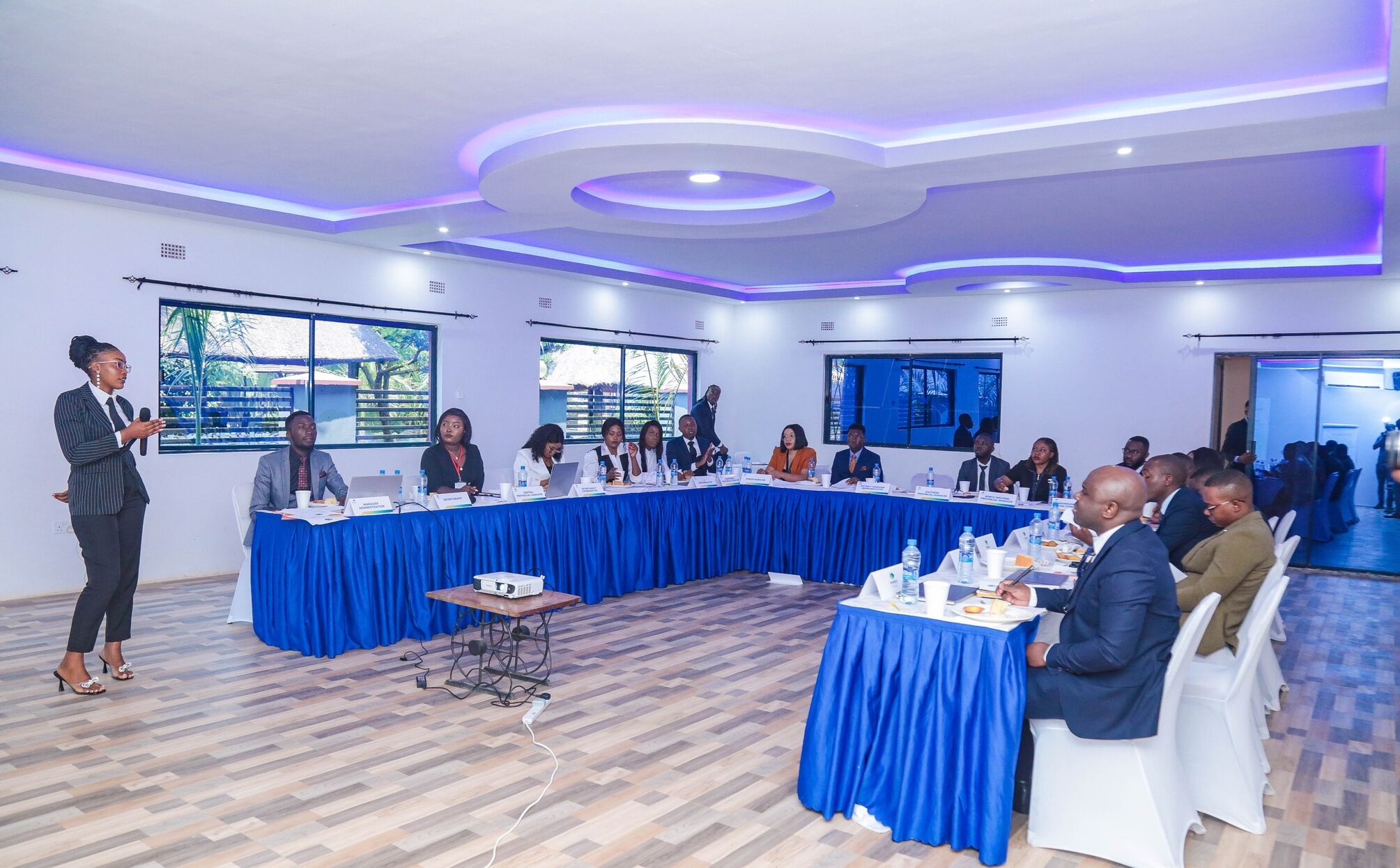 A conference room with a long table, attendees, and a speaker.