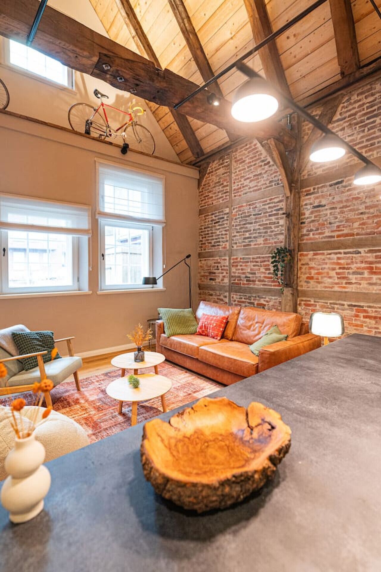 A cozy living room with a brick wall, a leather sofa, a round coffee table, and a bicycle mounted on the wall.