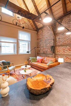 Een gezellige woonkamer met een bakstenen muur, een leren bank, een ronde salontafel en een fiets aan de wand.