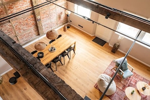 Ein Loft-Zimmer mit freiliegenden Backsteinwänden, einem Holztisch und Blick auf die Stadt durch große Fenster.