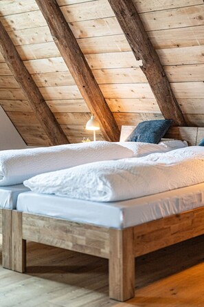 A wooden bed with white bedding in a room with exposed wooden beams on the ceiling.