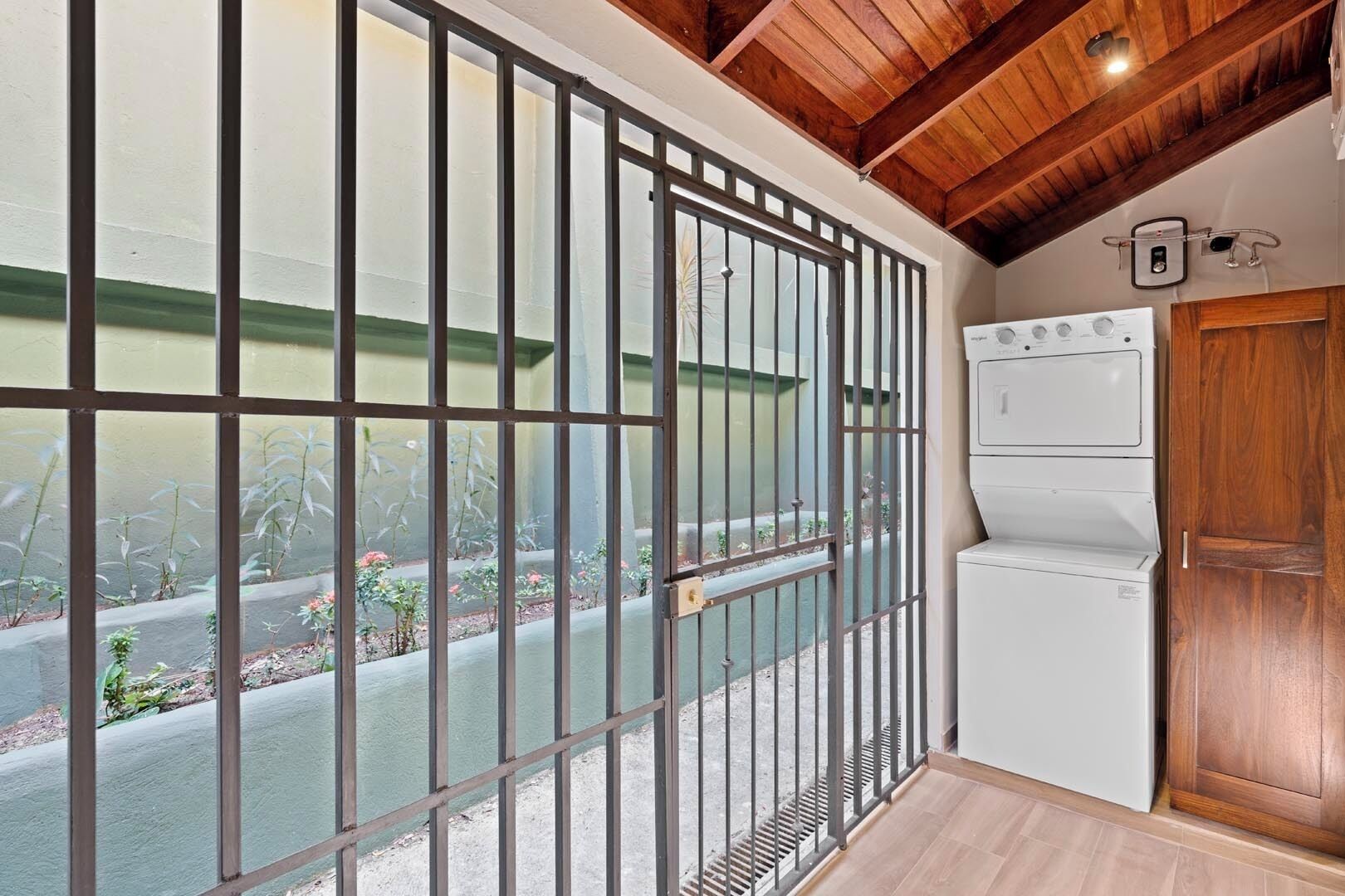 A room with a view through metal bars, a white refrigerator, and wooden ceiling beams.