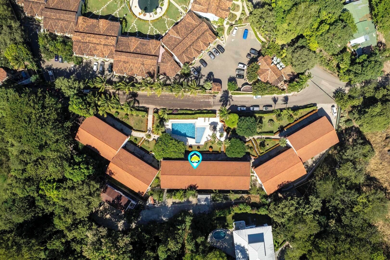 An aerial view of a resort with multiple bungalow-style buildings, a central swimming pool, and surrounding greenery.