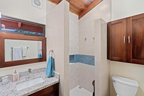 Een badkamer met een granieten aanrechtblad, een houten wastafelmeubel, een wit toilet en een douche met blauwe tegels.
