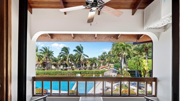 A balcony with a pool view, wooden ceiling, and a ceiling fan. - Stylish 2-Bedroom Beach Condo with Ocean-View Deck, Lush Pool Area & 2-Minute Walk to Flamingo Beach (Cabo Velas)