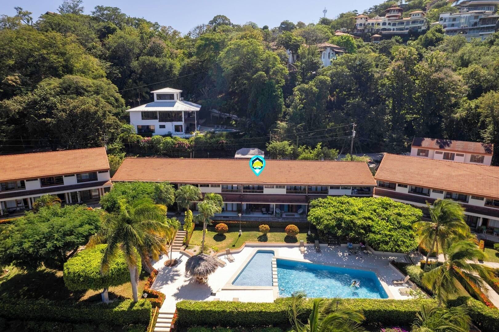 A resort with a swimming pool surrounded by lush greenery and palm trees.