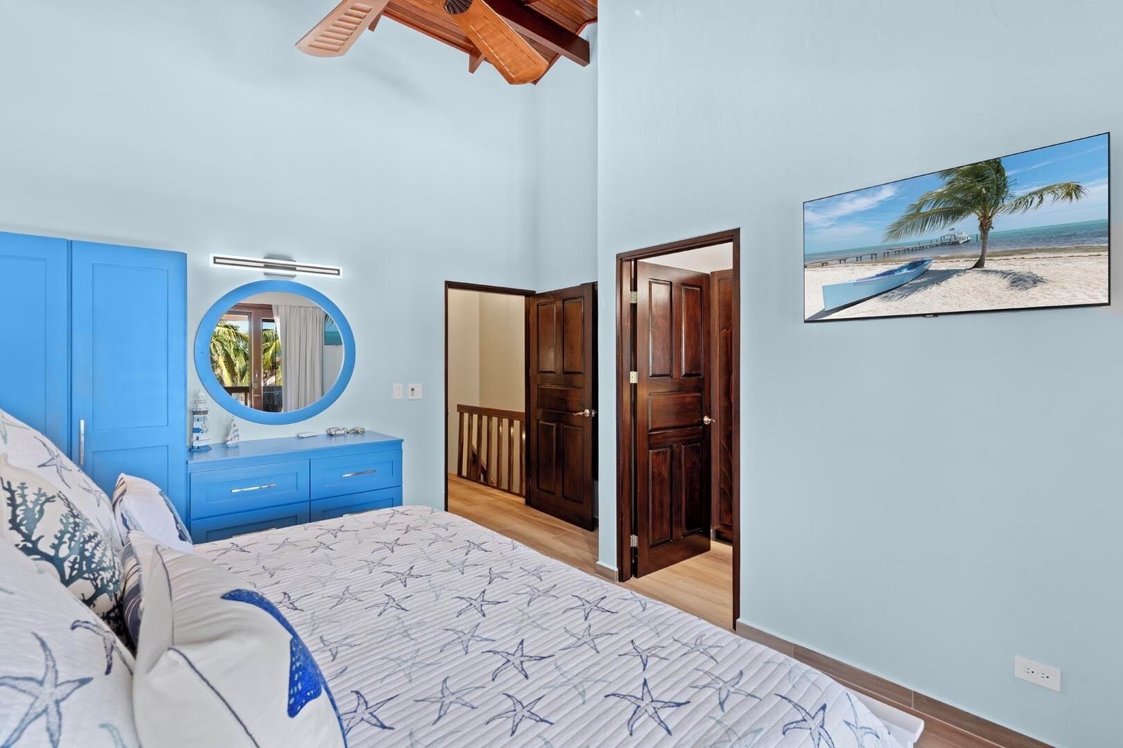 A bedroom with a bed, a blue dresser, a mirror, and a door leading to a balcony.