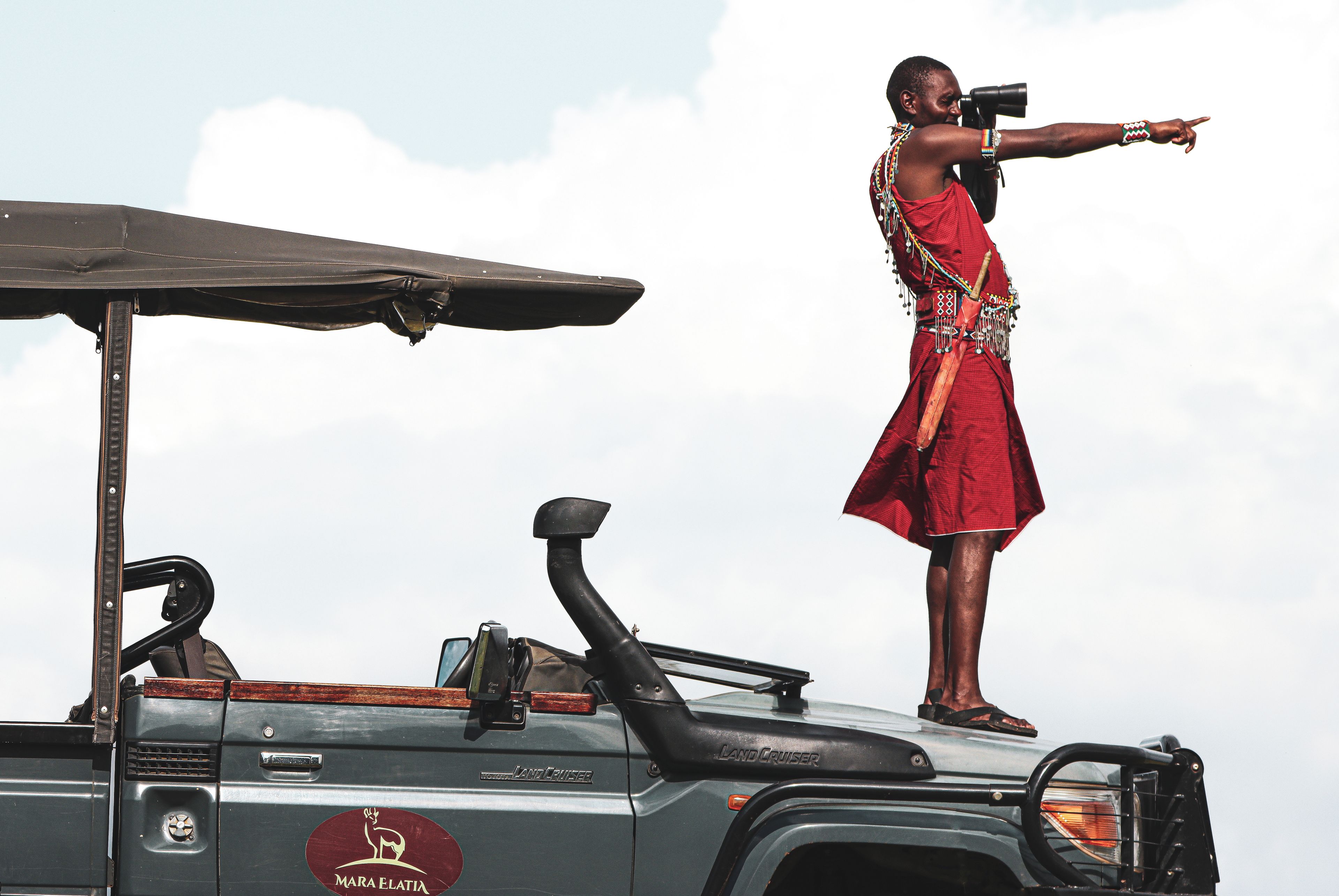 A person standing on a vehicle with a safari vehicle logo and a red patterned cloth.