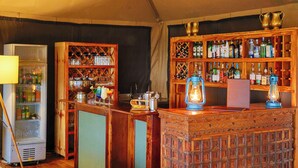 A bar area with a vintage design, including a wooden bar counter, shelves of liquor bottles, and a vintage lantern. - Mara Elatia Camp (Maasai Mara)