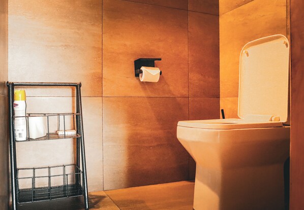 Un baño con inodoro, un perchero para toallas y artículos de aseo, y un dispensador de papel higiénico en la pared.