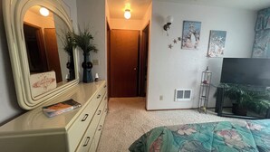 A bedroom with a large mirror, a dresser, a bed with floral bedding, a television, and a door leading to another room. - Beachfront Condo 3rd Floor Corner Unit sleeps 4, Spectacular Panoramic Ocean Vie (Seaside)