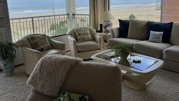 A living room with a view of the beach, featuring a sofa, armchairs, a coffee table, and a lamp. - Beachfront Condo 3rd Floor Corner Unit sleeps 4, Spectacular Panoramic Ocean Vie (Seaside)