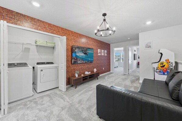 A laundry room with a brick wall, a television, and a sofa in a living area.