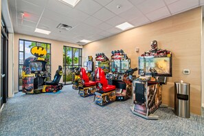 Une salle avec des jeux d’arcade, dont des machines sur le thème de Batman et de Terminator 2, et une grande fenêtre donnant sur des palmiers.