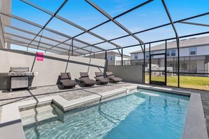 Una piscina interior con techo de cristal, sillas de descanso y una parrilla.