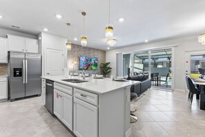 Une cuisine moderne dotée d’un îlot central, d’appareils électroménagers en acier inoxydable et de luminaires suspendus.