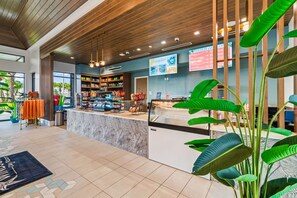 Un espace d’accueil moderne avec un plafond en bois, un comptoir doté d’une vitrine et diverses commodités, notamment un espace pour les boissons et un coin salon avec des chaises orange.