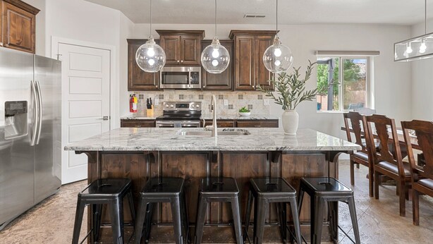 A kitchen with a large island, stainless steel appliances, wooden cabinets, and hanging pendant lights. - Lakeside Oasis at Sand Hollow: Private Pool + Private Hot Tub (Hurricane)