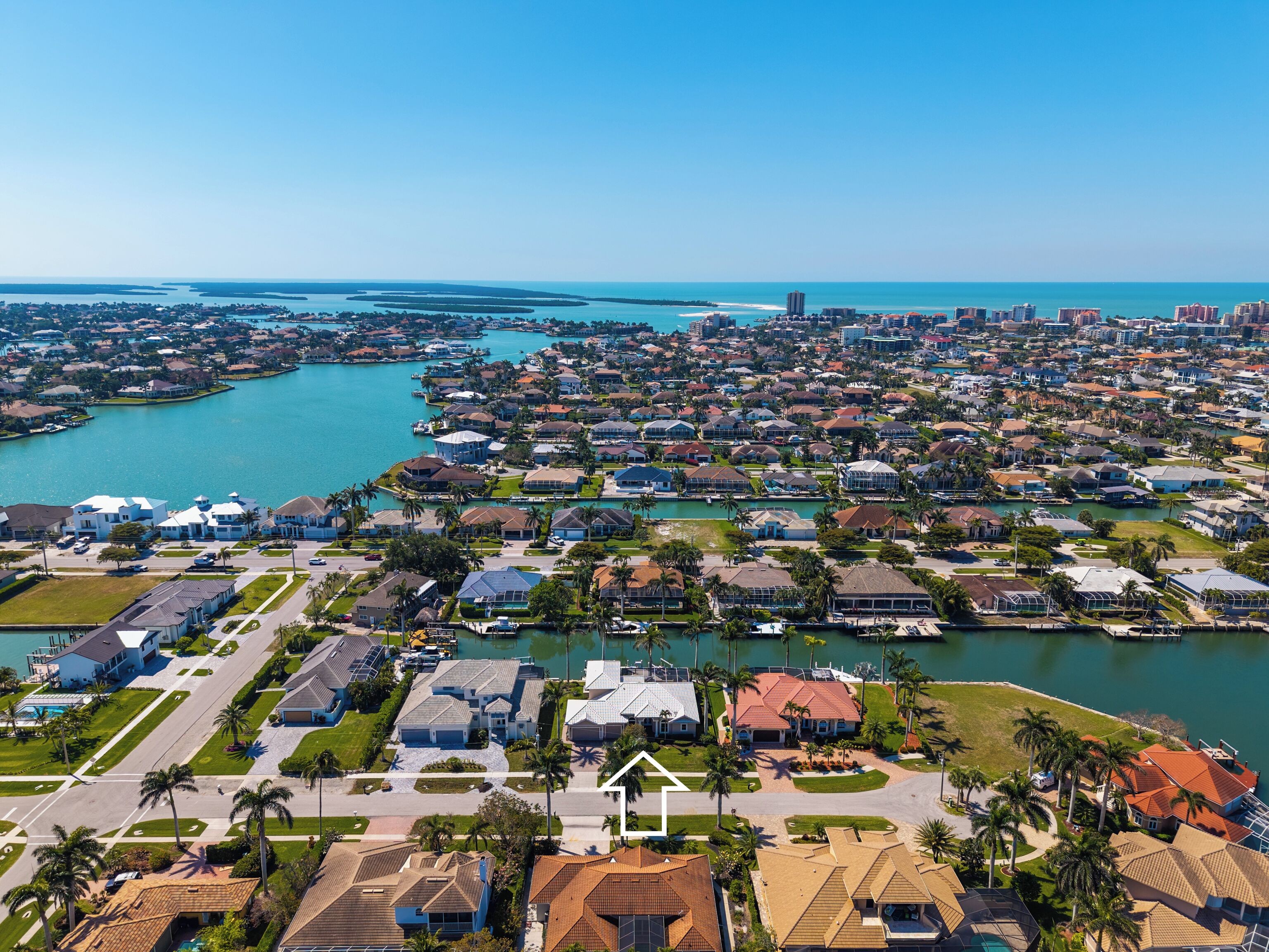 Vue aérienne d’une zone résidentielle côtière, avec des maisons, une marina et une vaste étendue d’eau.