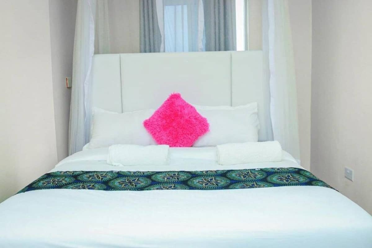 A neatly made bed with white linens, a decorative pillow, and a patterned bedspread.