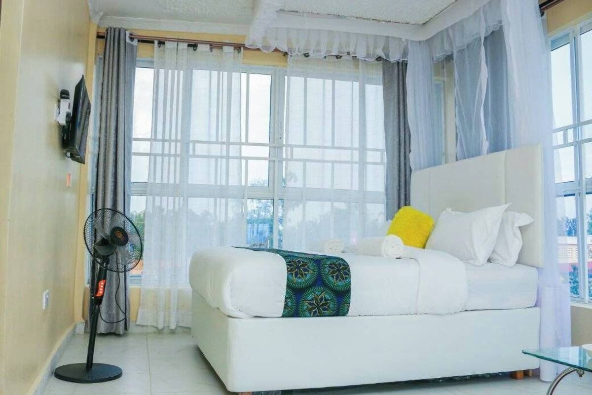 A bedroom with a bed, a standing fan, and a window with curtains.
